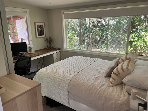 Une chambre à coucher avec un lit, un bureau, un ordinateur et une fenêtre donnant sur des arbres.