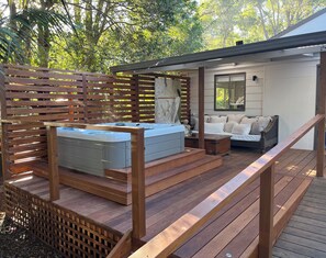 Une terrasse en bois avec un jacuzzi, un canapé et un escalier menant à un espace abrité doté d’une fenêtre et d’un miroir.