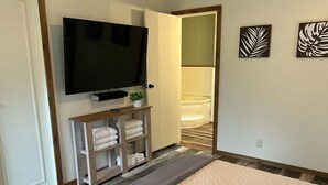 A hotel room with a bed, a TV mounted on the wall, a shelf with towels, and artwork on the wall.