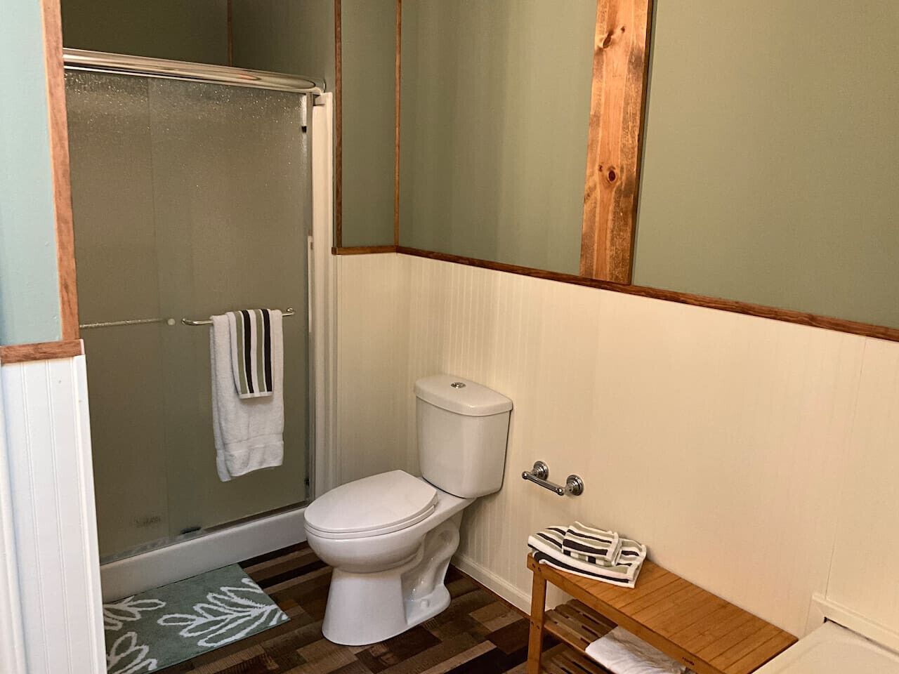 Une salle de bain avec une douche, des toilettes et un petit tabouret en bois.