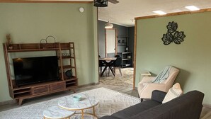 A living room with a sofa, a TV stand, a dining table, and a kitchen in the background.
