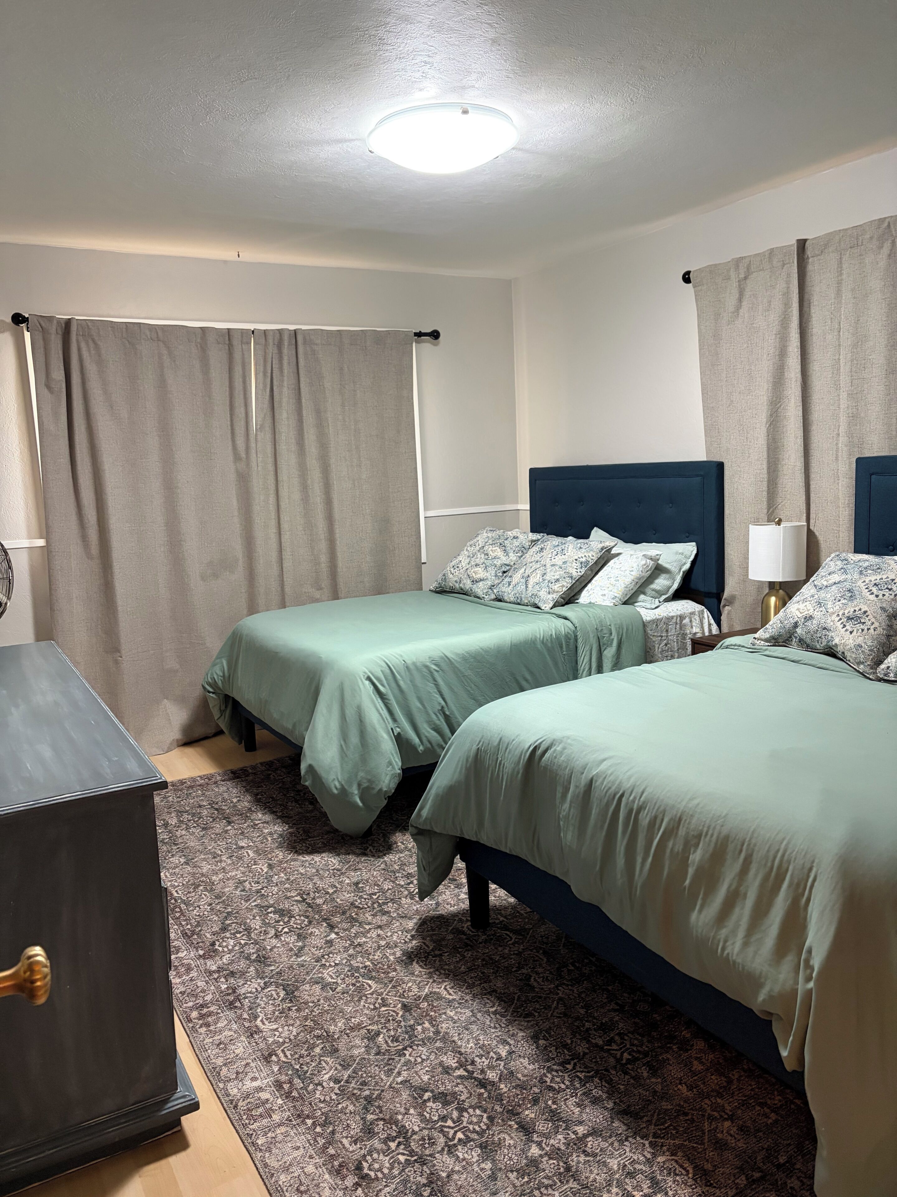 Hotellihuone, jossa on kaksi sänkyä, työpöytä, lamppu ja kuviollinen matto.