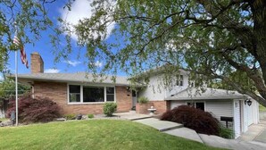 A two-story house with a brick facade, a front yard with a lawn and a small garden, and a clear blue sky. - Clarkston House with pool! Relax and enjoy with family and friends (Clarkston)