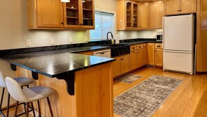 A kitchen with wooden cabinets, a black marble countertop, a white refrigerator, and two pendant lights. - Clarkston House with pool! Relax and enjoy with family and friends (Clarkston)