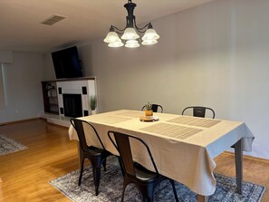 A dining area with a table set for four, chairs, a chandelier, a fireplace, and a television. - Clarkston House with pool! Relax and enjoy with family and friends (Clarkston)