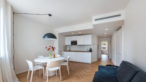 Een moderne keuken met witte kasten, een magnetron, en een eethoek met een witte tafel en stoelen.