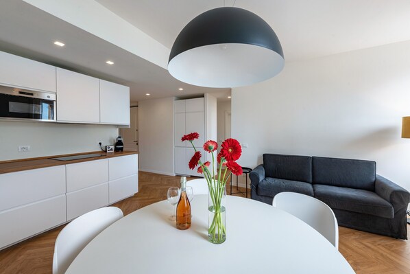 Una cocina moderna con armarios blancos, una lámpara colgante negra y un comedor con mesa y sillas blancas.