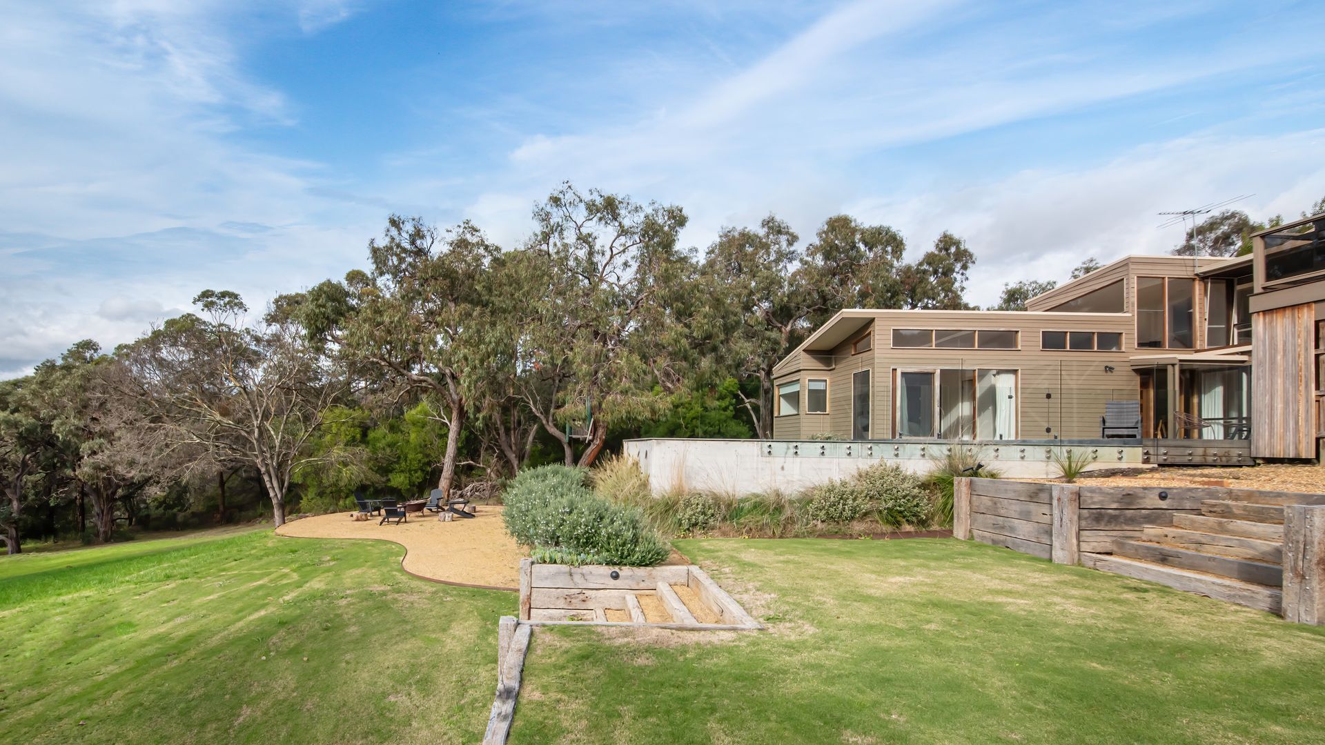 A modern two-story house with a large backyard, a wooden deck, and a swimming pool.