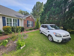 Ein weißer Kia Minivan vor einem Haus mit Backsteinfassade und weißem Putz.