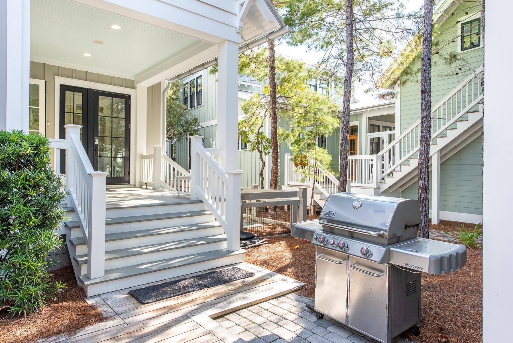 A covered porch with a grill, steps leading to a door, and a small garden area.