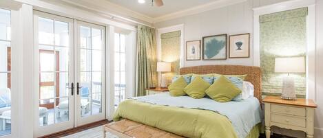 Un dormitorio con cama, un banco, un ventilador de techo, una mesita de noche, una lámpara y vistas al exterior a través de una puerta corrediza de vidrio.