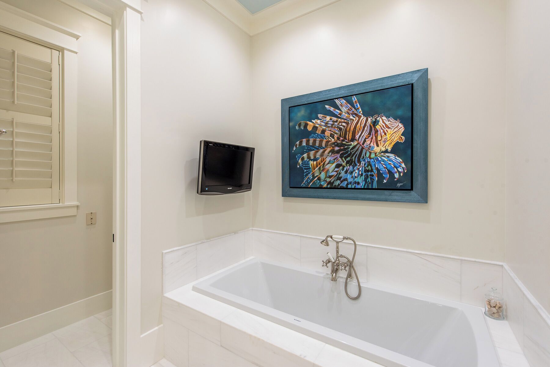 Une salle de bain moderne dotée d’une grande baignoire, d’un téléviseur à écran plat fixé au mur et d’une œuvre d’art colorée au-dessus de la baignoire.