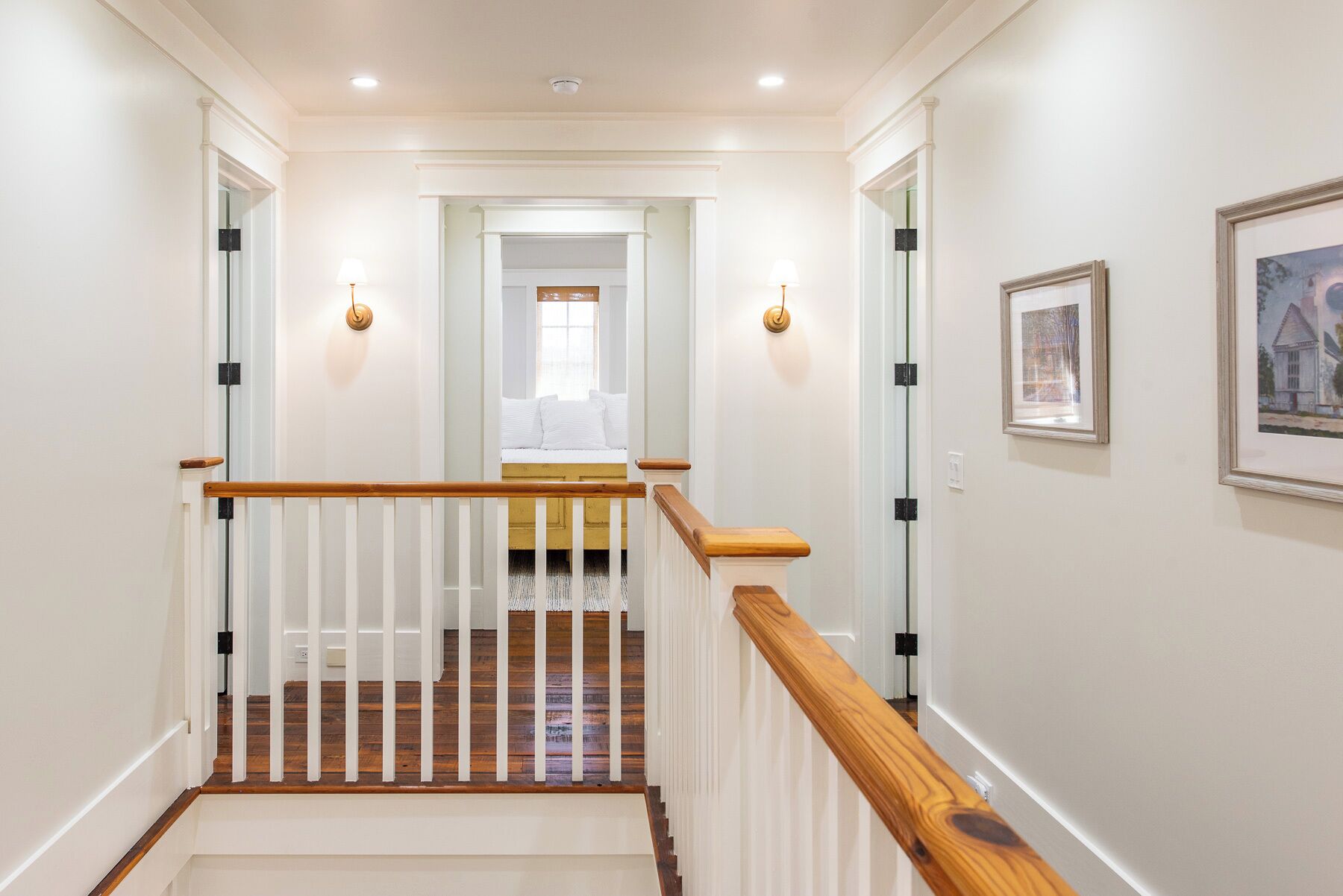 Una escalera con barandilla de madera y balaustres blancos que lleva a un dormitorio con cama y ventana.