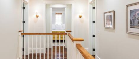 Una escalera con barandilla de madera y balaustres blancos que lleva a un dormitorio con cama y ventana.