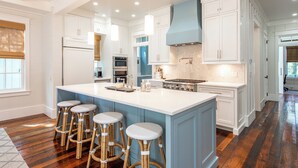 A spacious kitchen with a large island, white cabinetry, and a blue accent wall. - WaterColor Cottage with 6 seater golf cart + 6 bikes, 9 pools, beach access! (Santa Rosa Beach)
