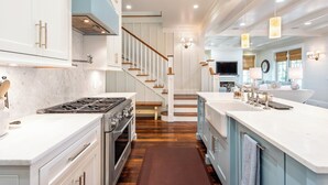 A modern kitchen with white cabinets, a central island, and a wooden staircase. - WaterColor Cottage with 6 seater golf cart + 6 bikes, 9 pools, beach access! (Santa Rosa Beach)