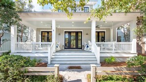 A two-story house with a covered porch, white railings, and a front door with glass panels. - WaterColor Cottage with 6 seater golf cart + 6 bikes, 9 pools, beach access! (Santa Rosa Beach)