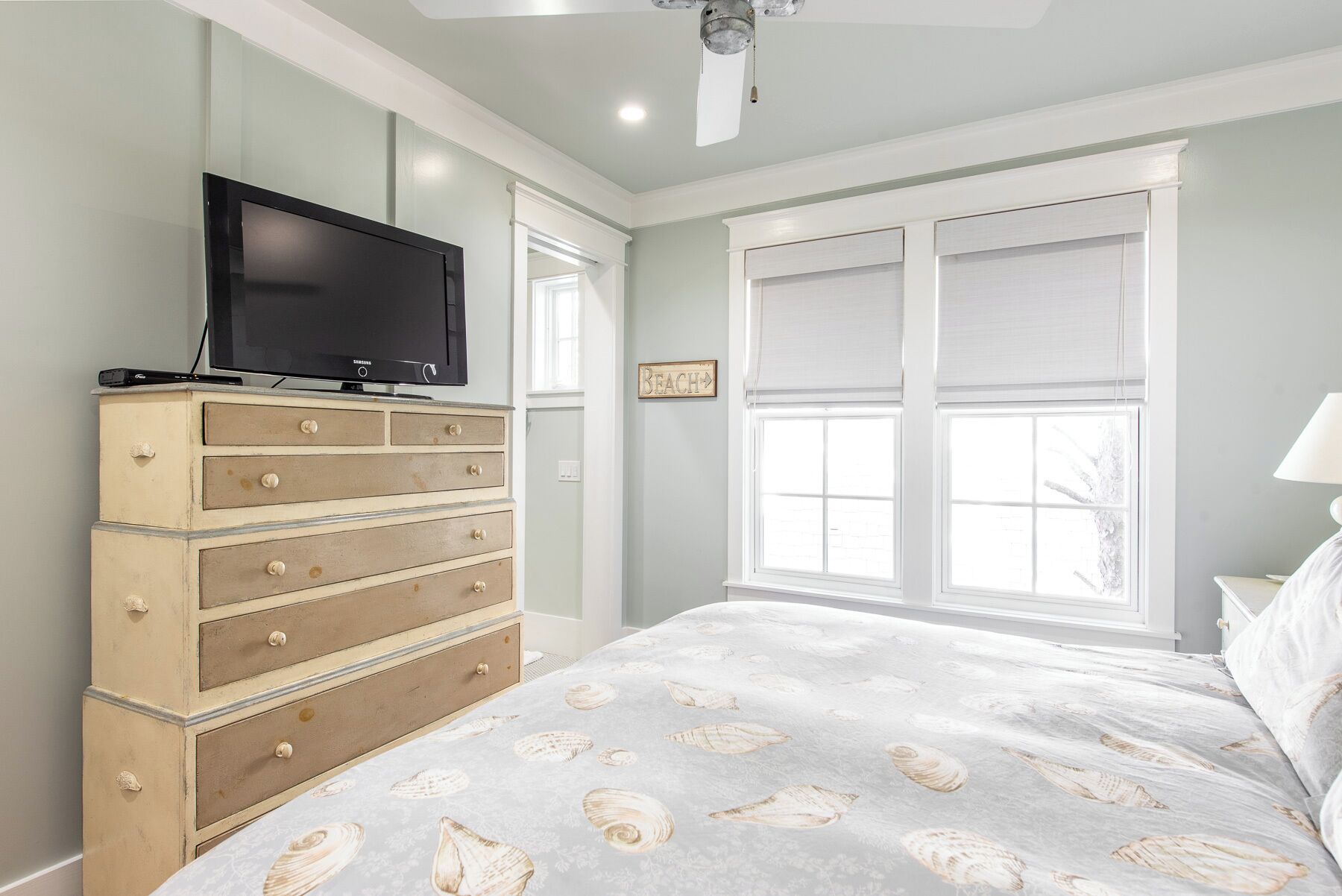 Een slaapkamer met een bed, een dressoir, een televisie en een raam met jaloezieën.