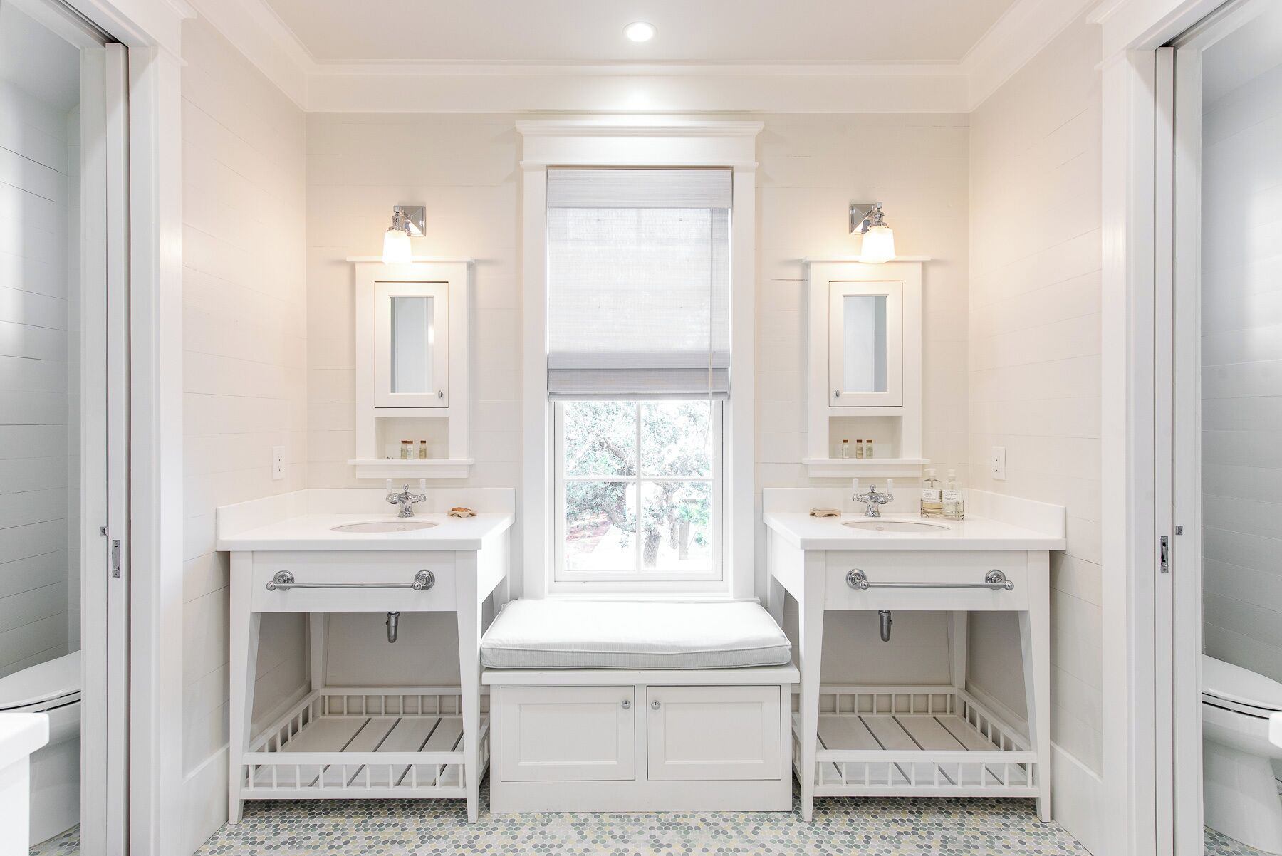 A bathroom with two sinks, a window, and a bench.
