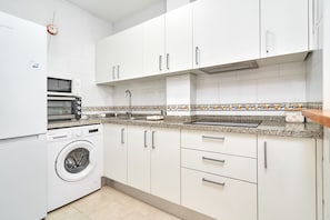 A kitchen with white cabinets, a washing machine, a microwave, and a sink.