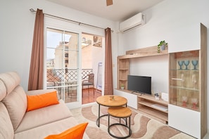 Un salon comprenant un canapé, un téléviseur, une petite table et une vitrine contenant des objets décoratifs.