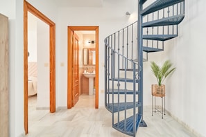 Un couloir avec une porte en bois donnant sur une salle de bain, un escalier en colimaçon bleu et une plante en pot.