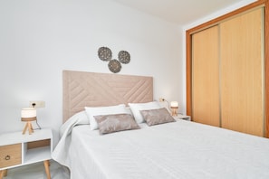 A bedroom with a bed, nightstands, a bedside lamp, a wooden wardrobe, and decorative wall art.