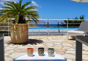 A terrace with a large potted plant, a pool, and two decorative cups on a table.