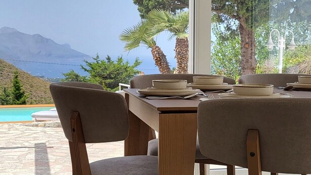 Un comedor con mesa y sillas, vista al mar y a las montañas, y una piscina exterior.