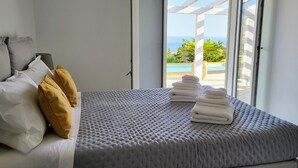 Un dormitorio con cama, almohadas, y ventana con vista a una piscina y follaje.