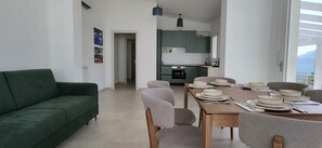 Una sala de estar moderna con un sofá verde, una mesa de comedor preparada para cuatro personas y una cocina al fondo.