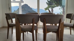 Habitación con vistas a las montañas y al mar, con cuatro sillas de madera y cojines grises.