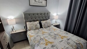 Une chambre à coucher avec un lit, deux tables de chevet, un ventilateur de plafond, une citation encadrée accrochée au mur et un tapis.