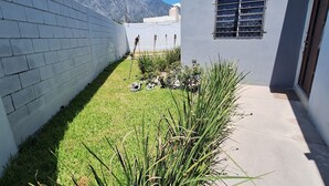 Un bâtiment moderne à l’extérieur en béton, avec un petit espace verdoyant agrémenté de plantes et une vue sur les montagnes en arrière-plan.