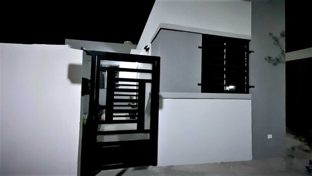 Une maison moderne avec une façade blanche, un portail noir et une fenêtre dotée de stores horizontaux.