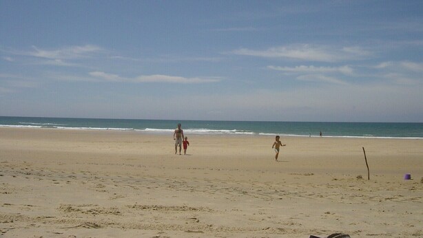 Ein Strand mit blauem Himmel, sandigem Ufer und Fußabdrücken.