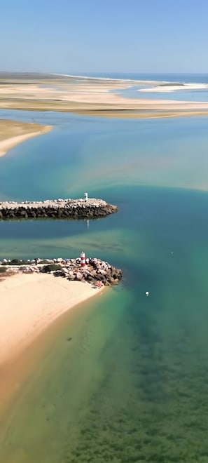 Eine Küstenlandschaft mit klarem Wasser, einem Sandstrand und einem Felsenmole mit Leuchtturm.