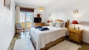 A bedroom with a bed, two bedside tables, a TV, a chair, a window, and a door. - Apartment 'Praia Da Rocha' with Balcony, Wi-Fi and Air Conditioning (Praia da Rocha)