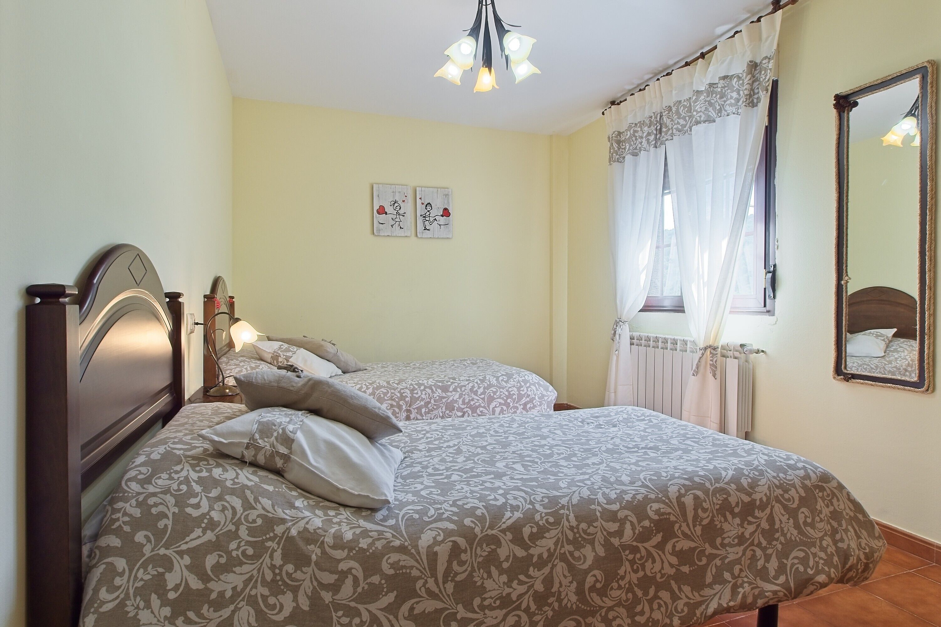 A bedroom with two beds, a ceiling light, a radiator, and two wall-mounted pictures.