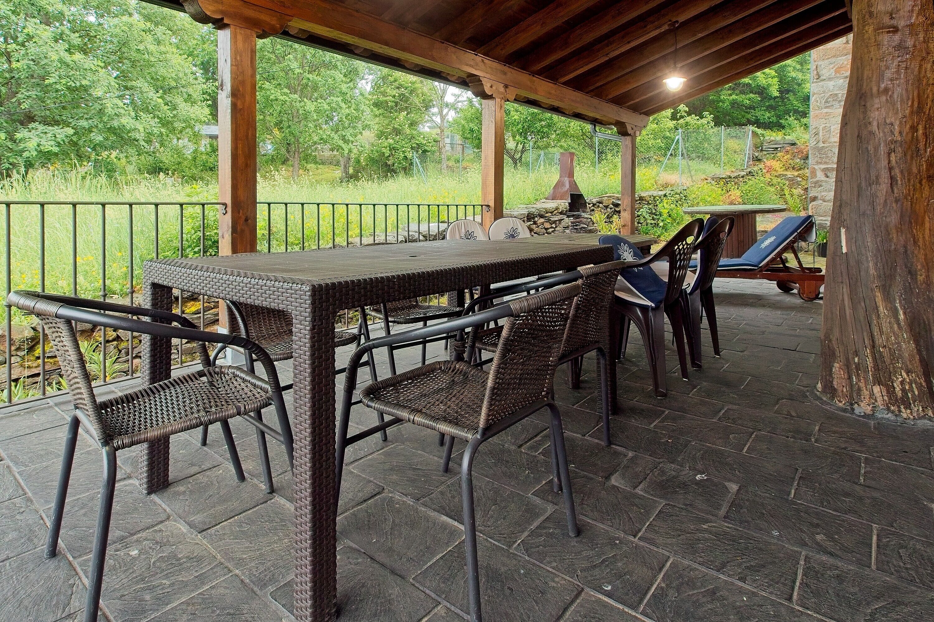 Une terrasse extérieure avec une table et des chaises, un sol en pierre et une vue sur la verdure.