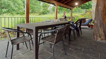 Un patio exterior con mesa y sillas, suelo de piedra y vistas a la vegetación.