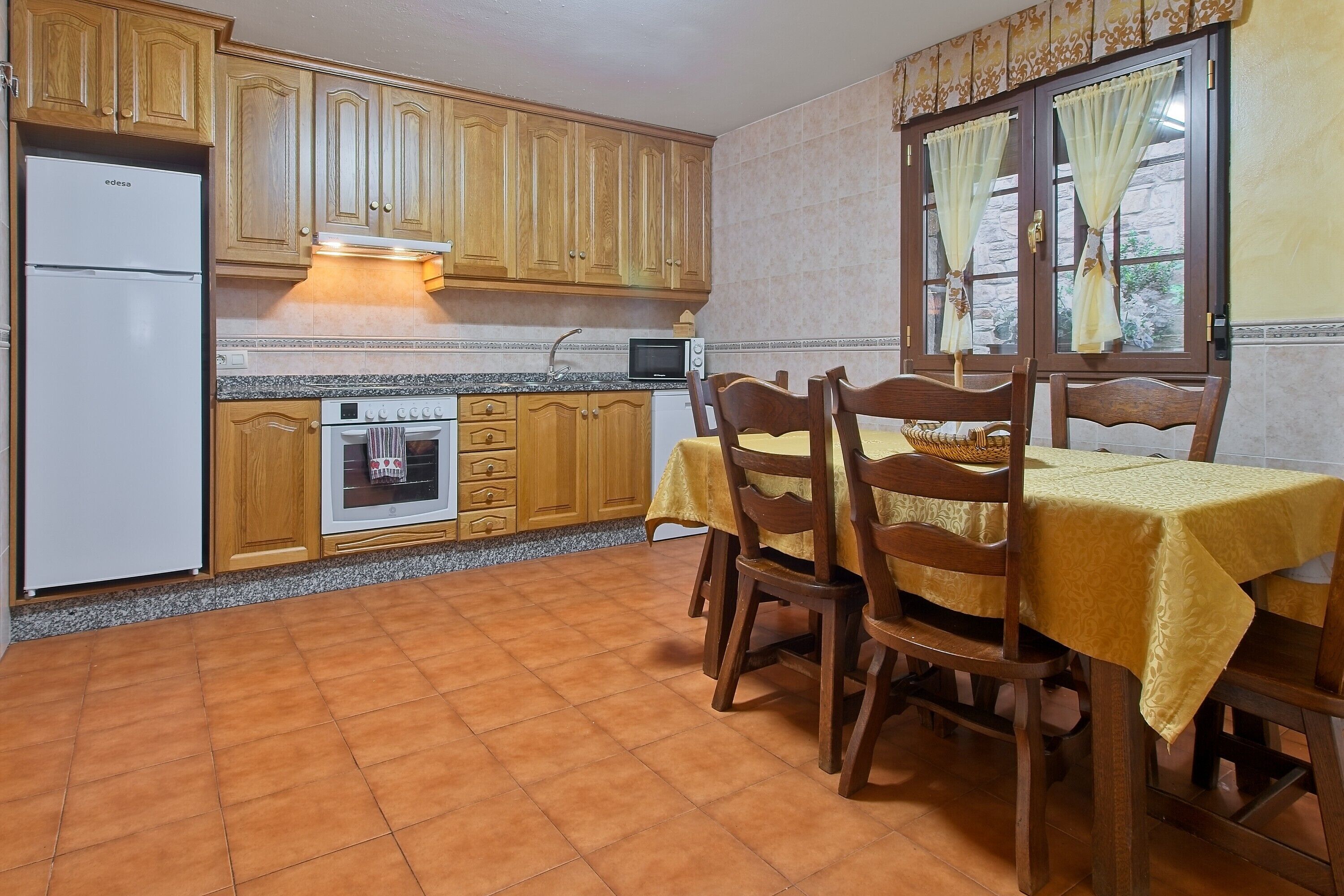 Une cuisine avec des meubles de rangement en bois, un réfrigérateur blanc, une cuisinière, un four à micro-ondes et une table à manger avec des chaises.