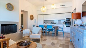 A modern living room with a TV, seating, and a dining area with chairs and a table.