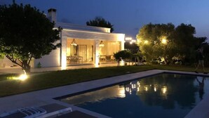 A modern house with an outdoor pool, a patio, and a well-lit interior.