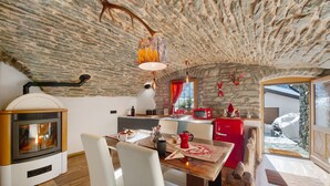 A rustic interior with a stone ceiling, a wood-burning stove, a dining area with a table and chairs, and a kitchen with a red refrigerator. - Apartment 'La Cachette' with Mountain View, Private Terrace and Wi-Fi (Aosta)
