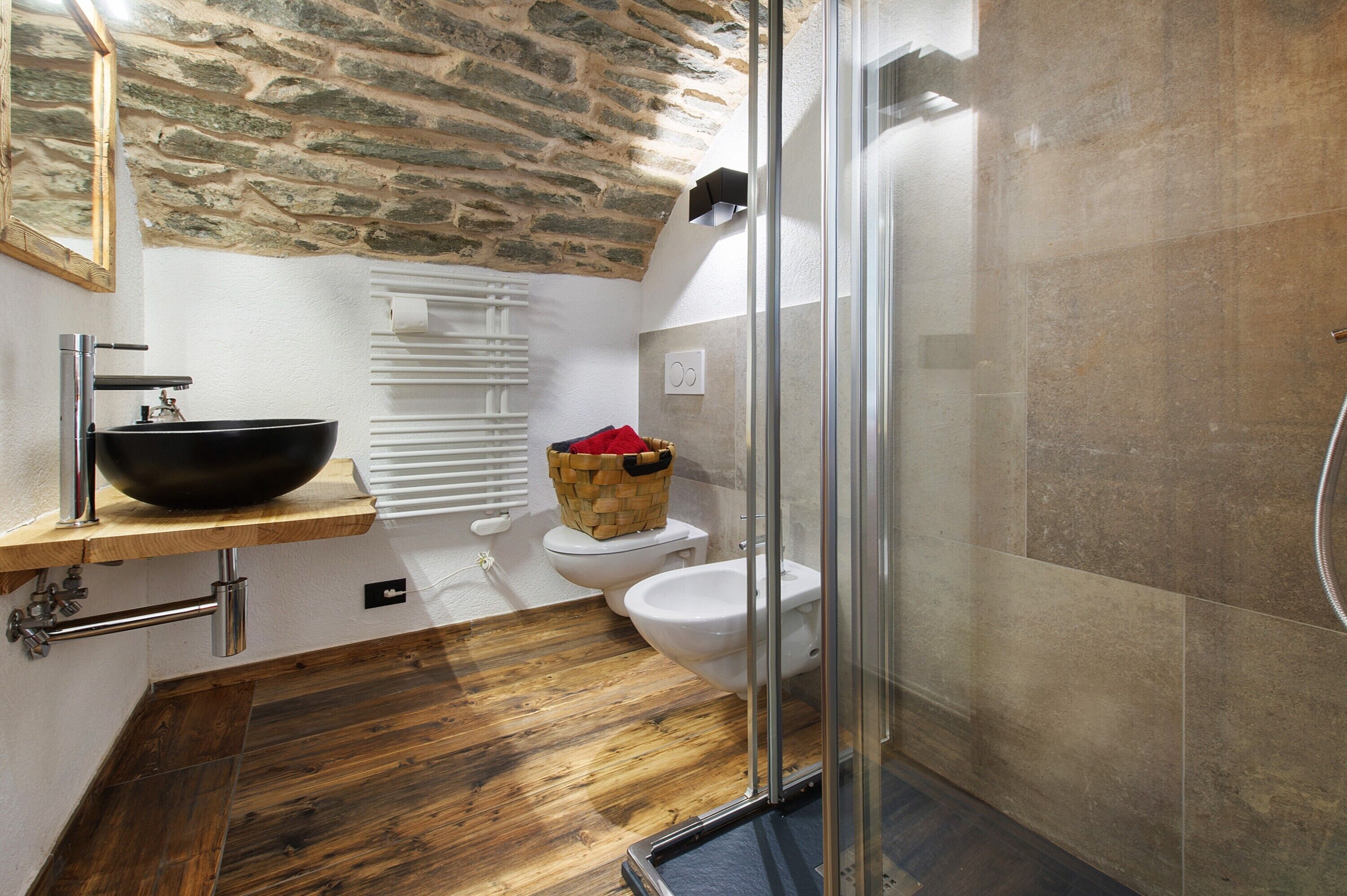 Ein Badezimmer mit einer Steinwand, einem schwarzen Waschbecken, einer weißen Toilette und einer Duschkabine aus Glas.