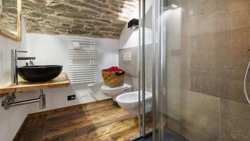 Ein Badezimmer mit einer Steinwand, einem schwarzen Waschbecken, einer weißen Toilette und einer Duschkabine aus Glas.