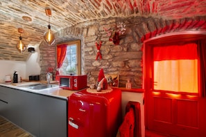 Una cocina con pared de piedra, un refrigerador rojo y una ventana con cortinas rojas.