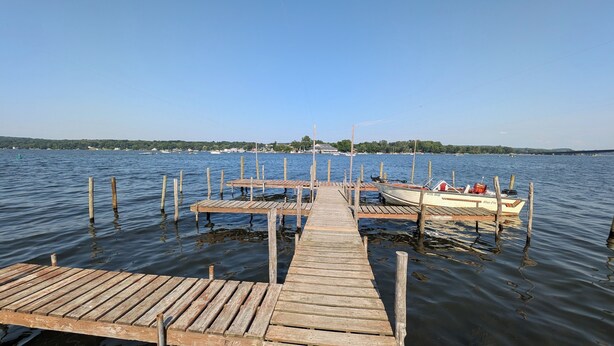 A wooden dock extending into a calm lake with a boat docked at the end. - Cottage #4 - Beautiful 3 Bedroom Lakefront Cottage - Fully Renovated in 2024! (Ashville)