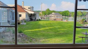 A view through a window of a grassy yard with a picnic table and a building in the background. - Cottage #4 - Beautiful 3 Bedroom Lakefront Cottage - Fully Renovated in 2024! (Ashville)